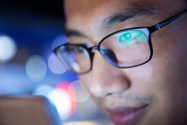 man looking at computer shows reflection of light in his glasses